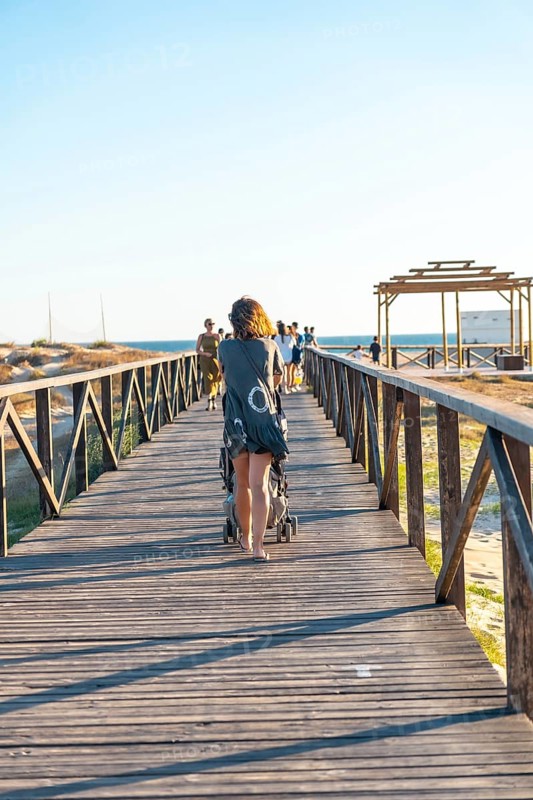A young mother walking on the walkway of the Bateles beach in Conil de la Frontera
