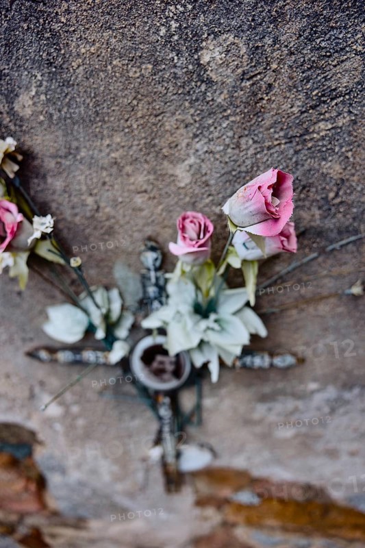 Artificial roses behind a cross on a weathered wall on a grave in a cemetery