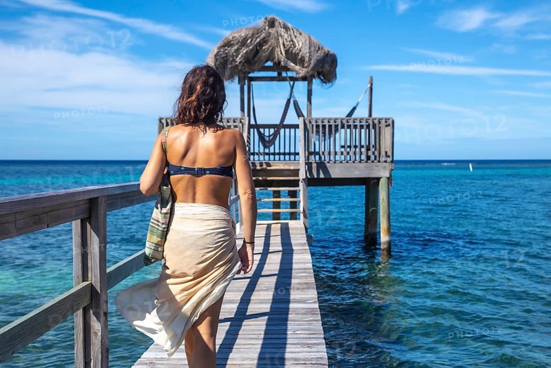 A young girl in a bikini walking to a wooden construction of the Caribbean Sea on Roatan Island. Honduras