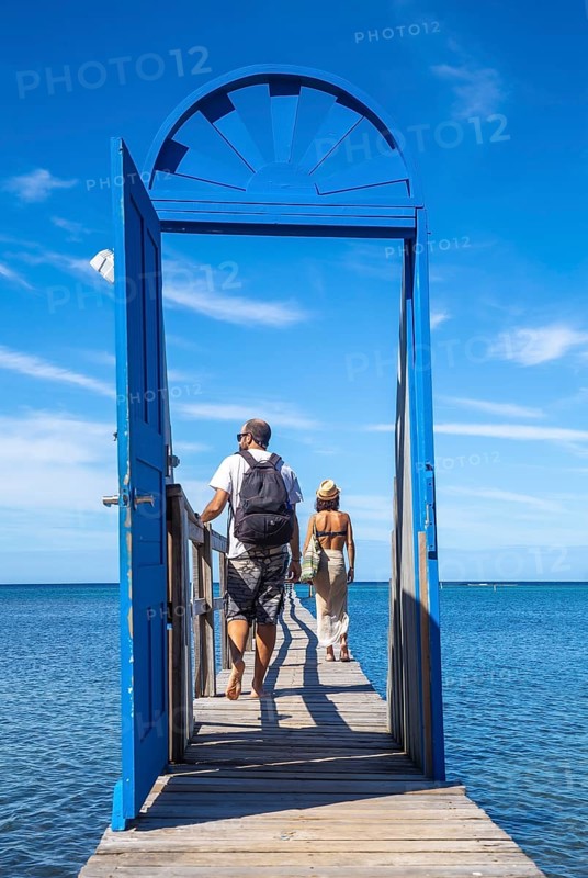 A couple at a blue door on the beach of Sandy Bay on Roatan Island. Honduras
