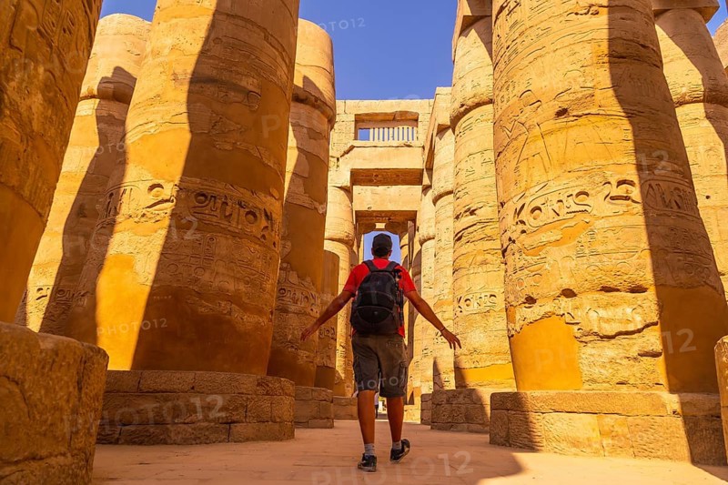 A young man walking between the columns with hieroglyphs inside the Karnak Temple