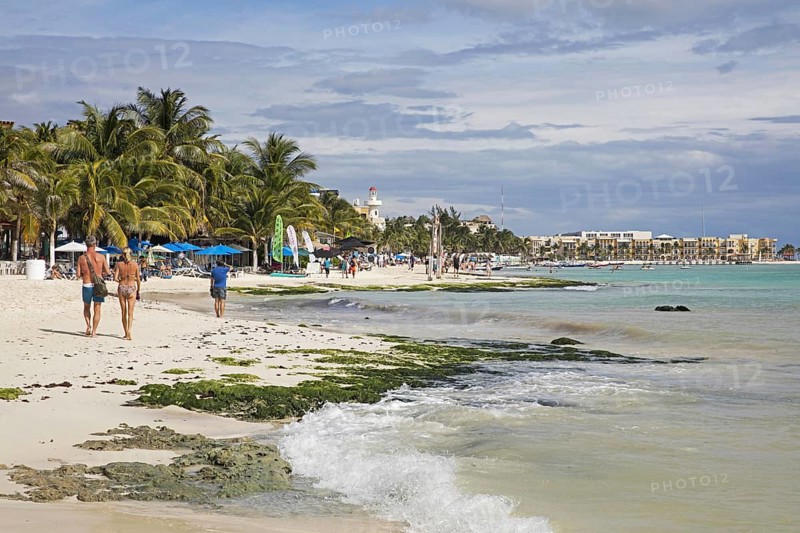 Western tourists walking on white sandy beach and hotels along Playa Del Carmen