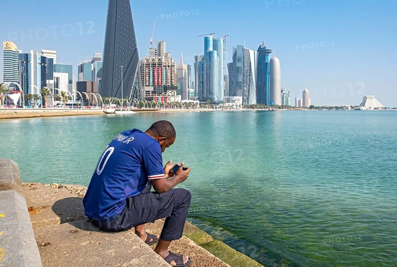 Man sits on steps of Corniche with skyscrapers in background