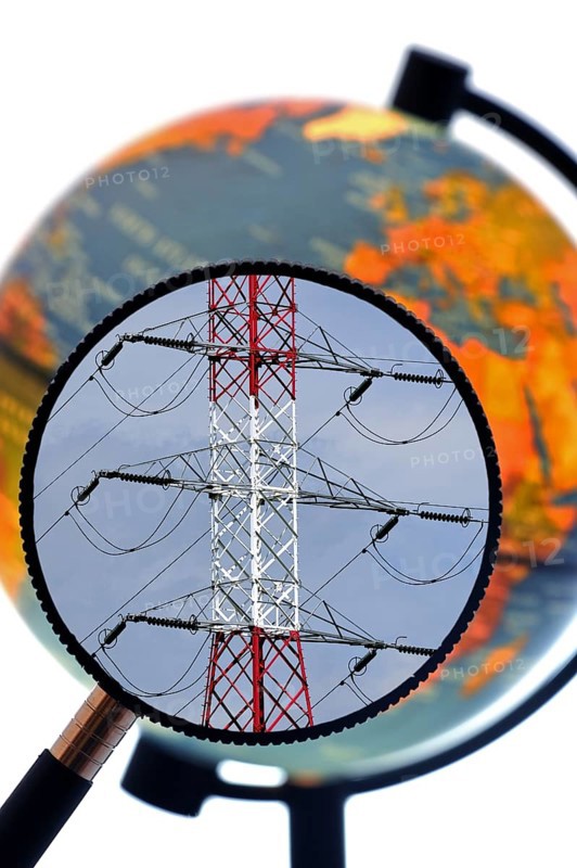 High voltage pylon in red and white through magnifying glass held against illuminated terrestrial globe