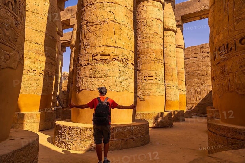 A young tourist walking among the columns with hieroglyphs inside the Karnak Temple