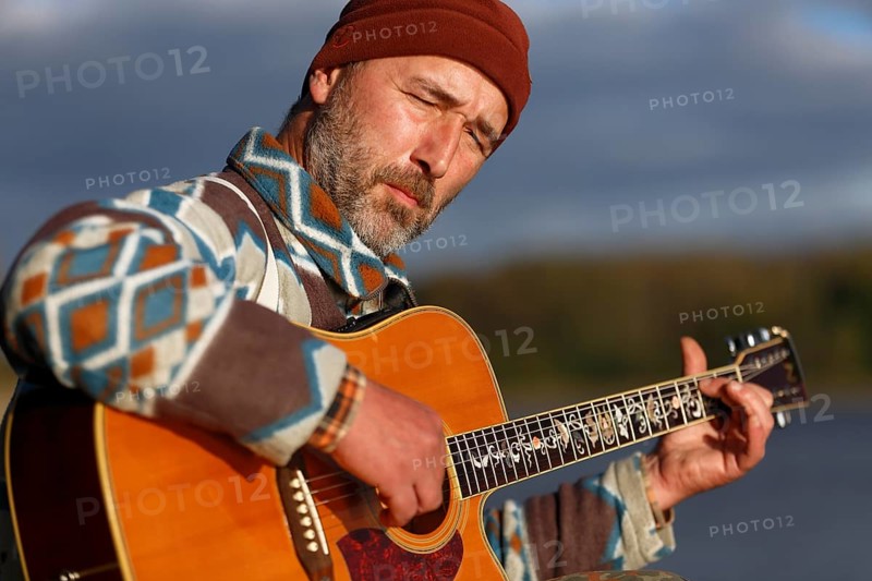 Man playing guitar on a jetty by the lake