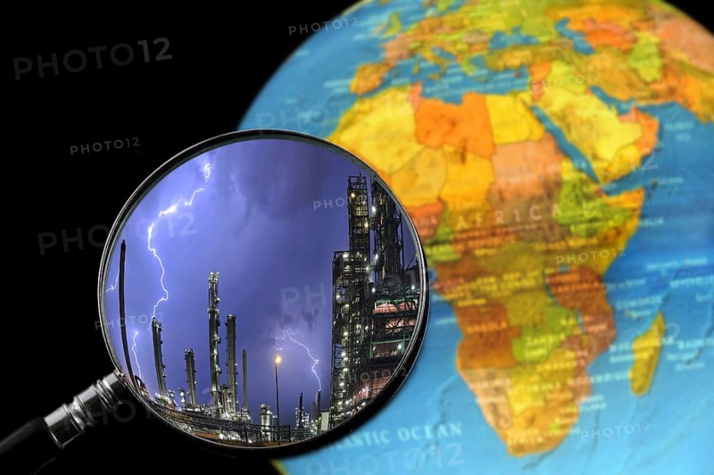 Lightning during thunderstorm above petrochemical industry seen through magnifying glass held against illuminated terrestrial globe