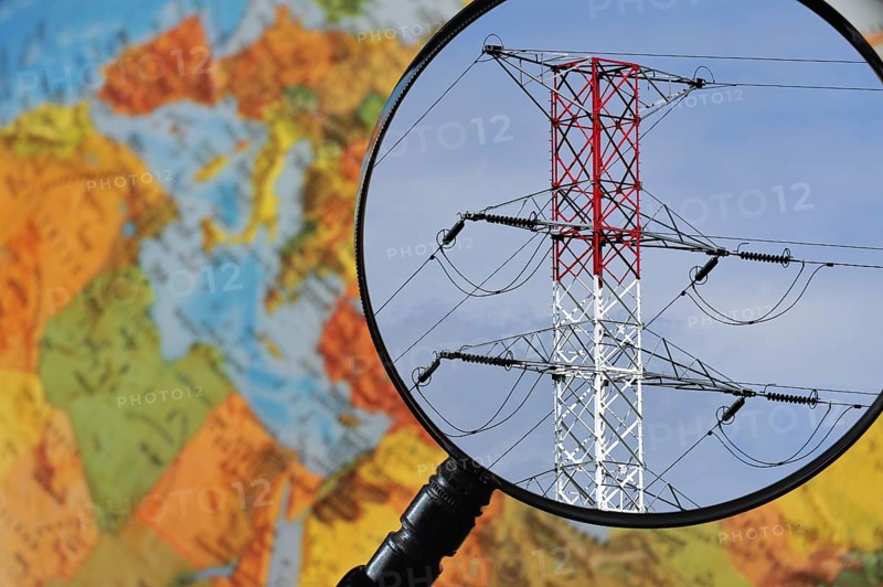 High voltage pylon in red and white through magnifying glass held against illuminated terrestrial globe