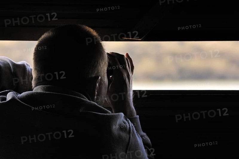 Bird watcher in hide looking through binoculars at waterfowl on lake in the nature reserve Parc du Marquenterre at the Bay of the Somme