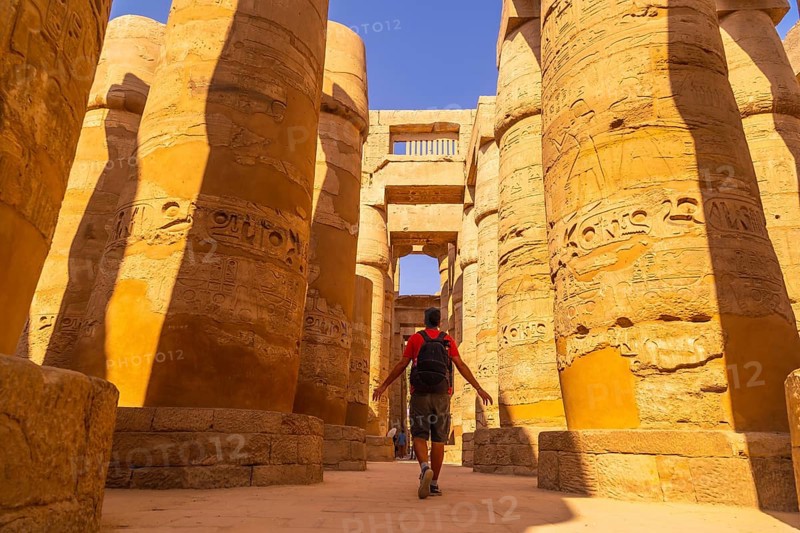 A young man walking between the columns with hieroglyphs inside the Karnak Temple
