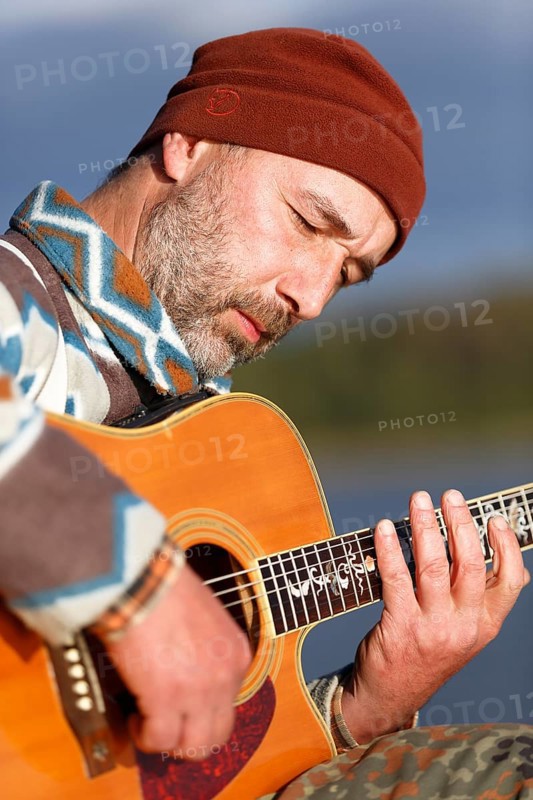 Man playing guitar on a jetty by the lake