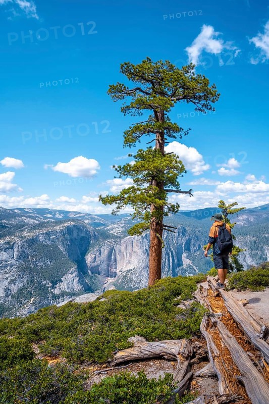 A young man with a brown jacket in Sentinel Dome looking at Upper Yosemite Fall