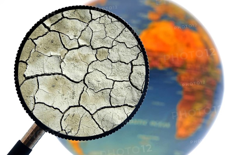 Cracked earth by drought seen through magnifying glass held against illuminated terrestrial globe