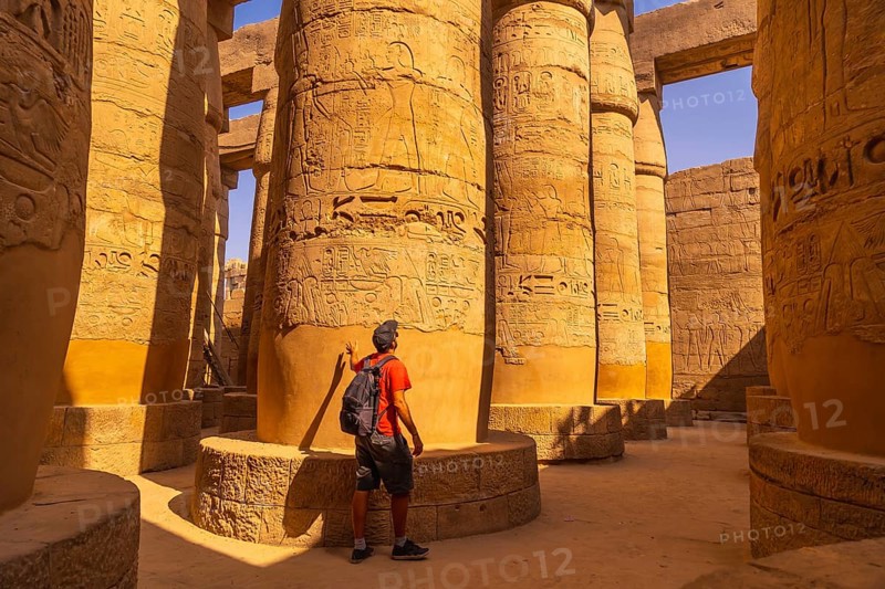 A young tourist walking among the columns with hieroglyphs inside the Karnak Temple
