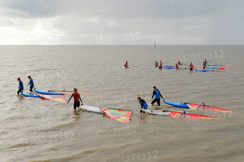 Surfers of a surf school pull the surfboard through the sea in the rain