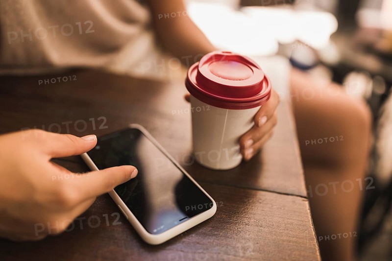 Close up girl browsing smart phone holding disposable cup