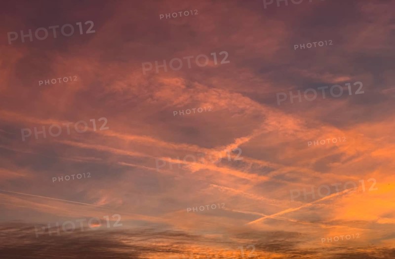 Coloured reddish orange sky Evening sky at dusk with veiling clouds Cirrostratus and contrails from air traffic Passenger aircraft