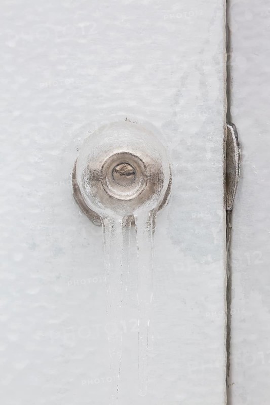 Close-up of ice covered doorknob with keyhole and strike plate on white door