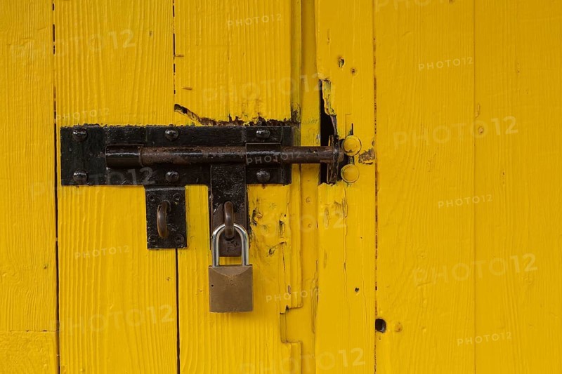 Yellow painted wood plank barn door locked with brass padlock