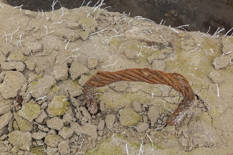 Handle shaped rusted steel cable encased in crumbling concrete block