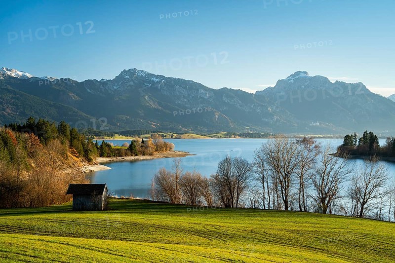 The Illasbergsee in the Allgäu in autumn in the late afternoon in good weather with a blue sky. A small hut in the foreground