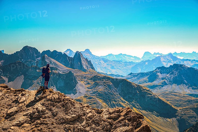 A hiker stands on the summit of the Mohnefluh in the Lechquellen mountains in Austria and looks over the Alps