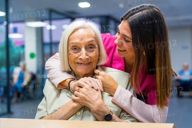 Nurse embracing from the back a cute elder woman in a geriatric
