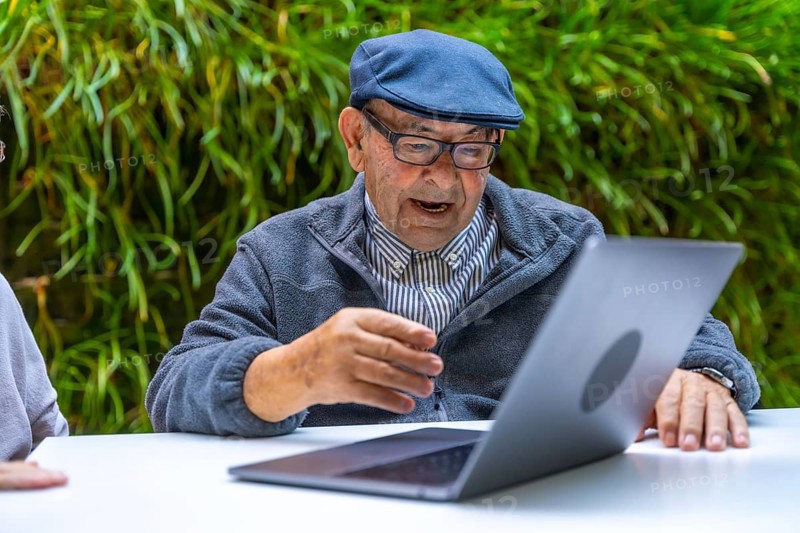 Retired old man using laptop in a garden of a nursing home