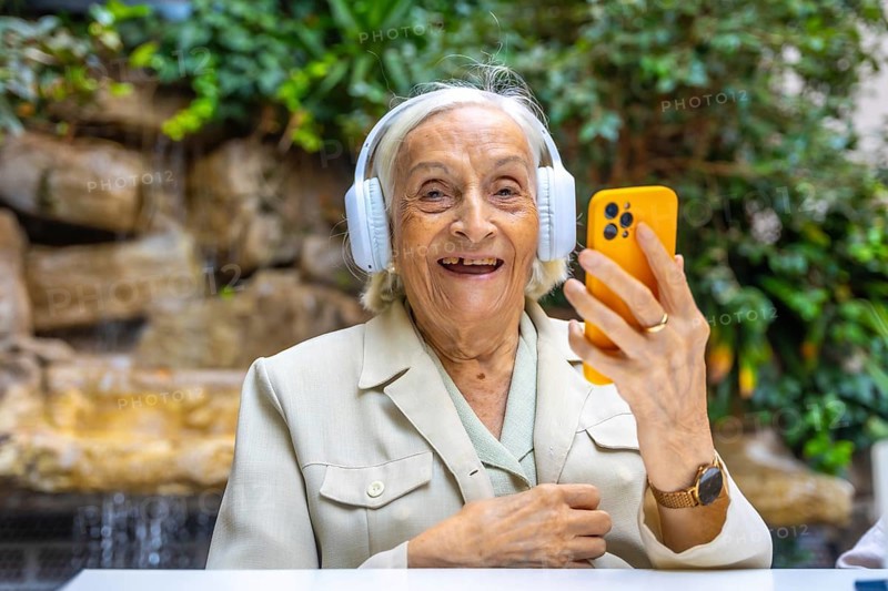 Happy elder woman using headphones and mobile to listening to music in a geriatric