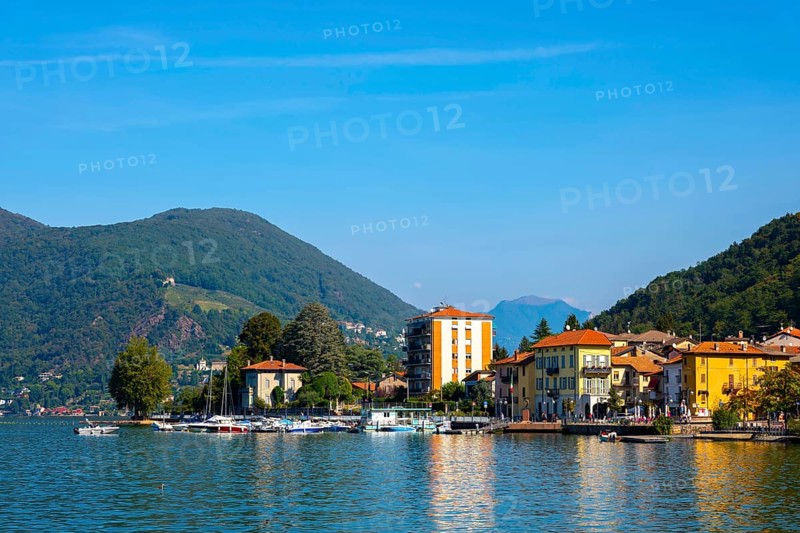 City of Porto Ceresio on Waterfront with Mountain and Lake Lugano in a Sunny Summer Day in Porto Ceresio