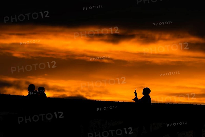 A passer-by takes a photo with her smartphone from the Eiserner Steg in Frankfurt am Main towards the sunset.