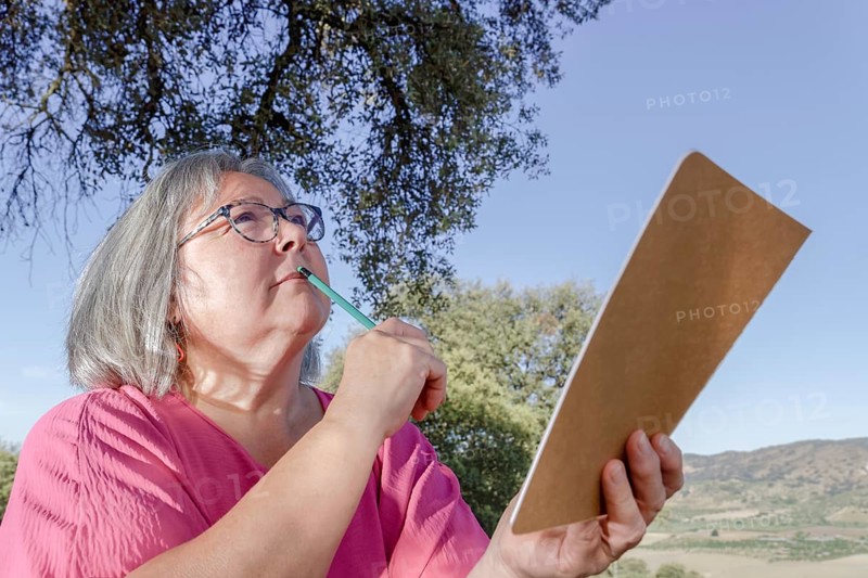 Older white-haired woman with a pencil on her lips and a notebook in her hand