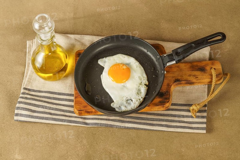 Fried egg with extra virgin olive oil in a frying pan with a glass bottle with oil on a wooden board