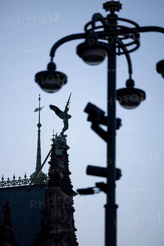 Angel figure with sword on the roof of the town hall fighting against a pole with lamps and video cameras
