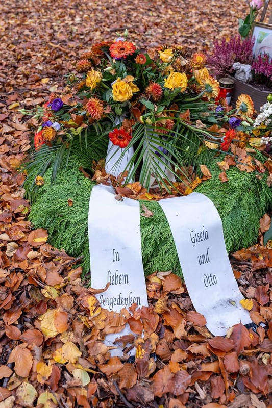 Flower wreath with mourning bows on autumn leaves at a memorial tree with the names of those buried there in Seelwald