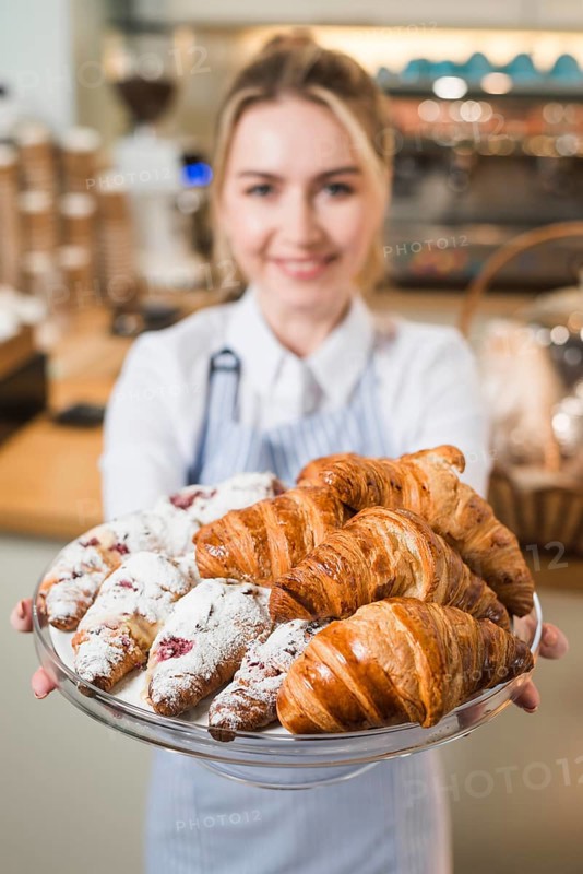 Blurred young woman offering croissants glass cake stand