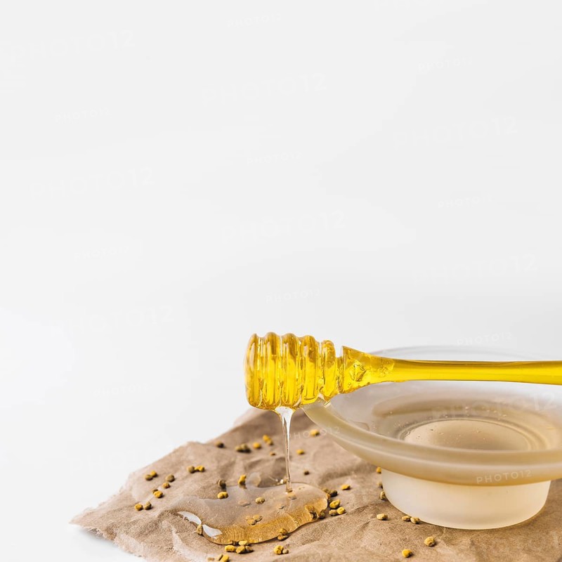 Close up sweet honey dripping from dipper with bee pollen seeds brown paper