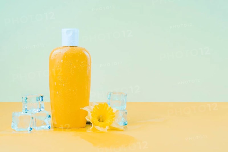 Crystal ice cubes with daffodil flower yellow sunscreen lotion bottle against green backdrop