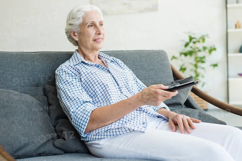 Elderly woman watching television using remote