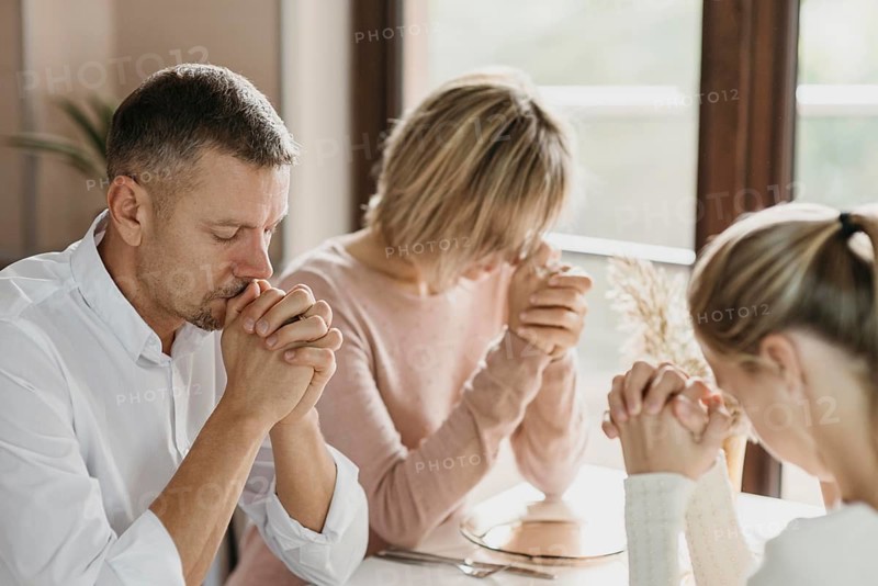 Family praying together before eating indoors