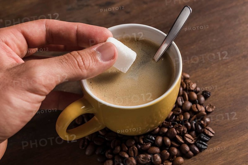 Hand holding sugar near cup with coffee