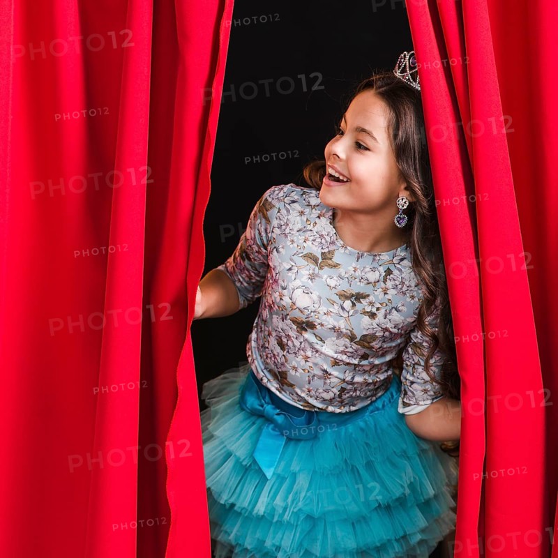 Happy girl peeking from red curtain stage