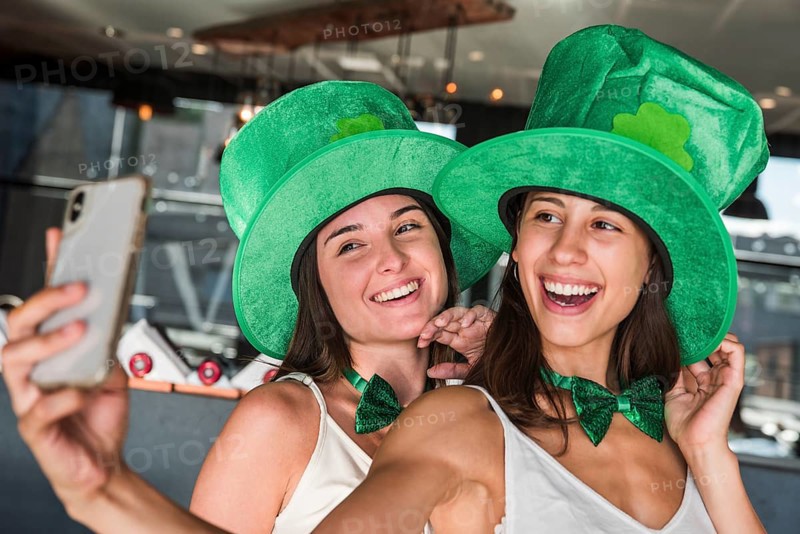 Happy young women saint patricks hats taking selfie smartphone