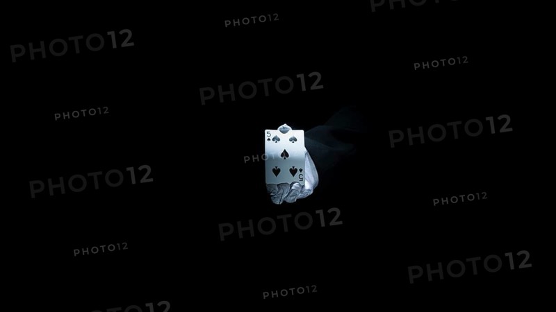 Magician s hand showing club playing card against black background