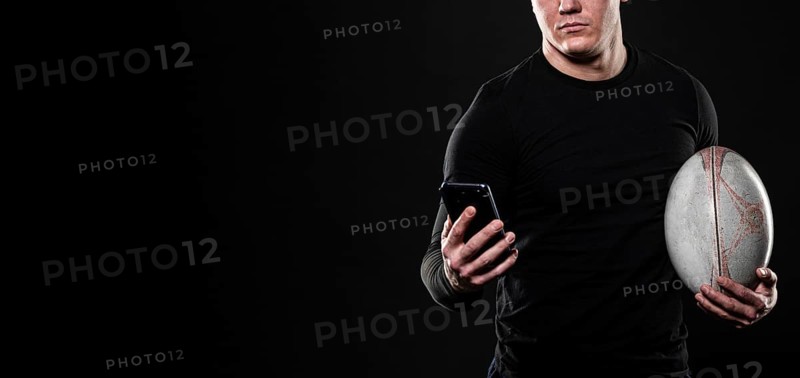 Male rugby player using smartphone while holding ball with copy space