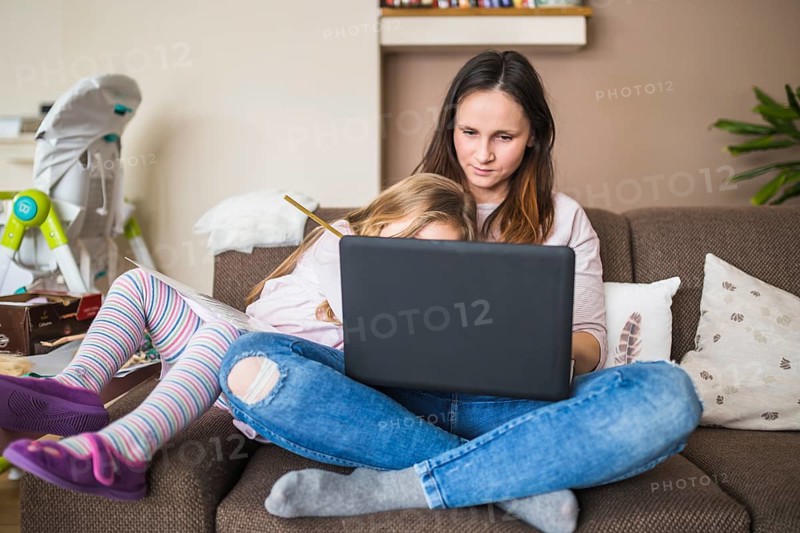 Mother with her daughter sitting sofa using laptop