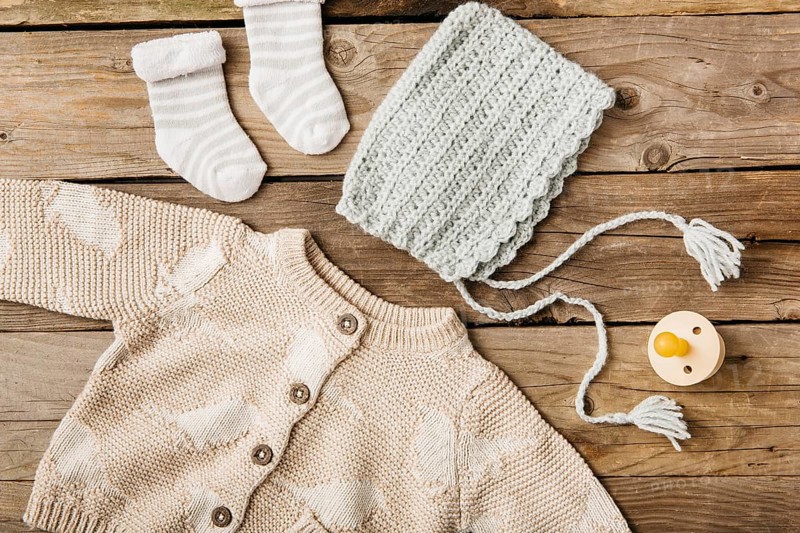 Overhead view woolen baby s clothing with pacifier wooden table
