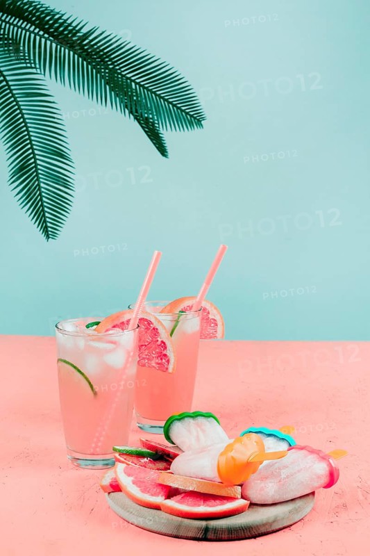 Palm leaves grapefruit cocktail glasses popsicles coral desk against teal background