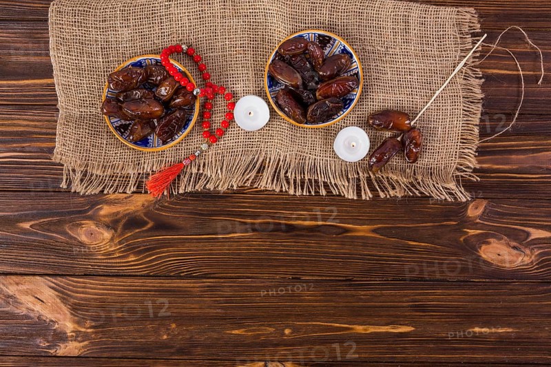 Plate juicy dates with red prayer beads lighted candle wooden desk