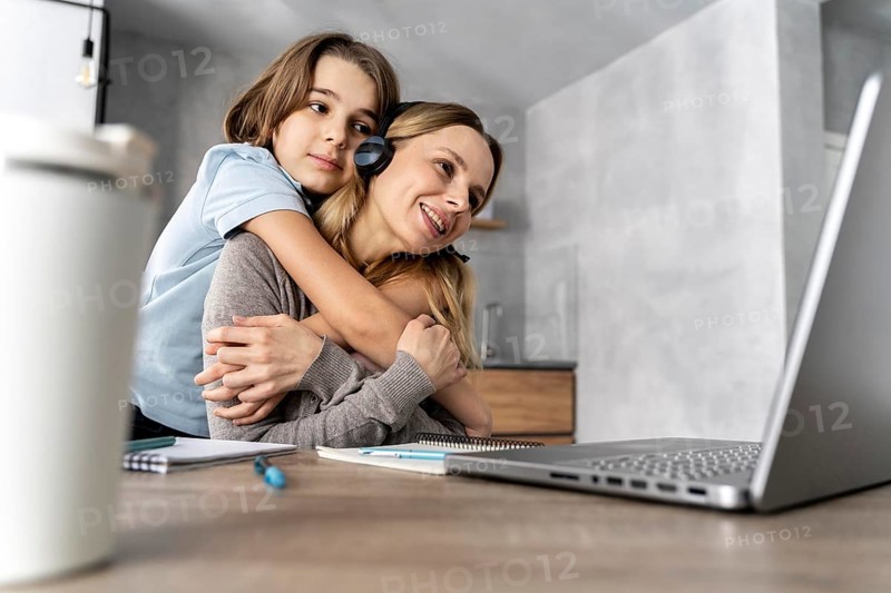 Woman with headset working laptop hugged by girl